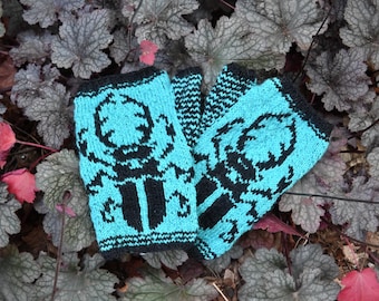 May include: A pair of turquoise fingerless gloves with a black pattern. The gloves are knitted and feature a repeating design. The gloves are resting on a bed of gray and red leaves.