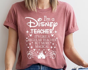 Könnte beinhalten: Ein T-Shirt in der Farbe Heather Mauve mit einer weißen Grafik, auf der "Ich bin ein Disney-Lehrer. Es ist wie ein normaler Lehrer, aber magischer." steht. Die Grafik enthält auch ein Disney-Schloss und Mickey-Maus-Ohren.
