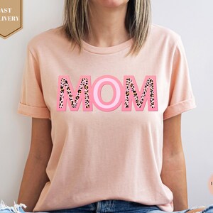 a woman wearing a pink mom shirt with leopard print