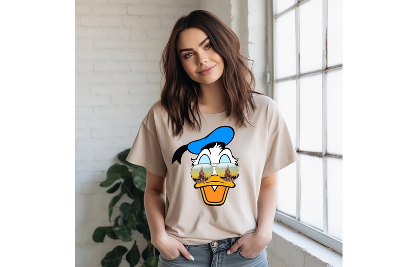 a woman standing next to a window wearing a t - shirt with a donald duck