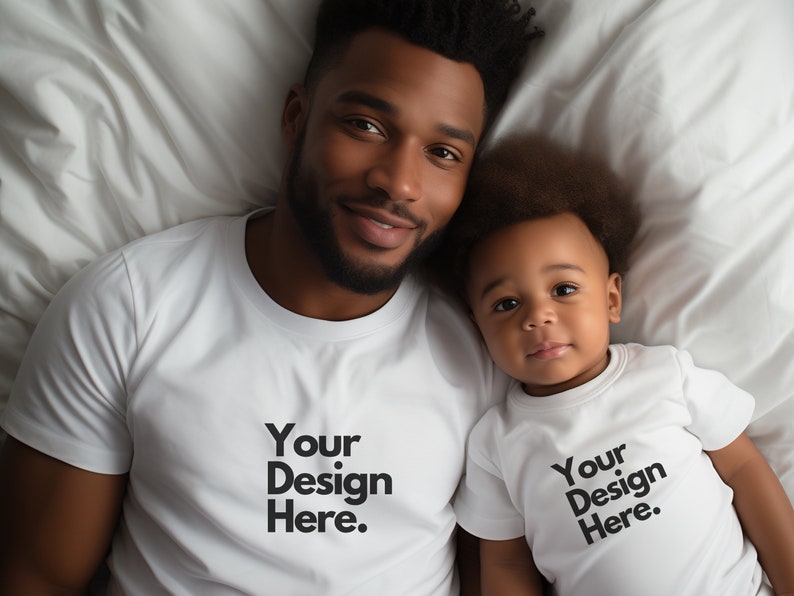 May include: A father and son wearing white t-shirts with the text "Your Design Here." printed on them. They are lying on a white bed.