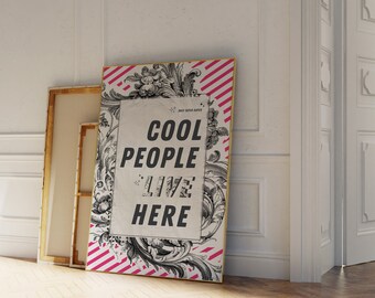 May include: A white poster with black text that reads "Cool People Live Here" on a pink and white striped background with black floral designs. The poster is leaning against a white wall.