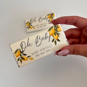 May include: A white chocolate bar wrapper with a lemon design. The wrapper says "Oh Baby" with the text "Baby Portelli Due May 2024".
