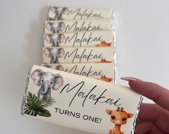May include: A white chocolate bar with a jungle animal theme. The bar has a picture of an elephant, a giraffe, and green leaves. The text on the bar reads "Malakai Turns One!"