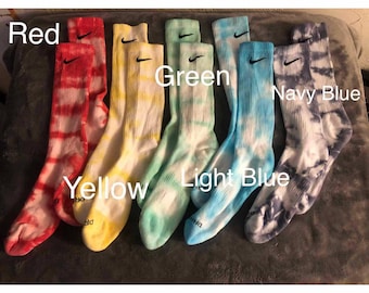 Puede incluir: Una colección de calcetines deportivos teñidos con tinte anudado en varios colores, incluyendo rojo, amarillo, verde, azul claro y azul marino. Cada par presenta el logotipo de Nike. Las palabras "Red", "Yellow", "Green", "Light Blue" y "Navy Blue" están escritas en la imagen.