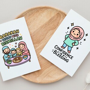 May include: Two white cards with colorful illustrations and text. One card says "Barakah begins with Bismillah" with a family illustration. The other card says "Confidence is a Blessing" with a cartoon character. Both cards are on a wooden tray.