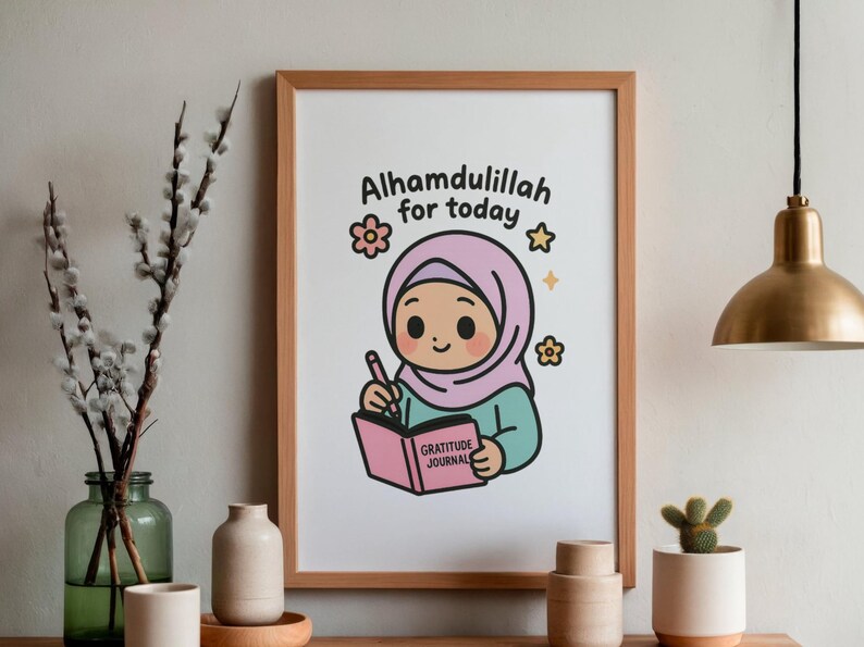 May include: A framed print featuring an illustration of a cartoon girl wearing a pink hijab, writing in a pink "Gratitude Journal." The text "Alhamdulillah for today" is above the girl. The print is in a wooden frame.