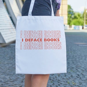 May include: A white tote bag with the text "I DEFACE BOOKS" repeated four times in a red and pink font.