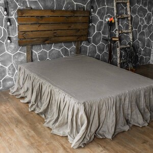 Può includere: Una balza per letto color beige con un design a volant arricciati che ricade sui lati della struttura del letto. Il tessuto ha un aspetto testurizzato e copre la base del letto, estendendosi dal materasso fino al pavimento in uno stile plissettato.
