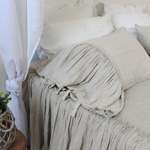 Puede incluir: Una falda de cama de lino gris claro con un borde con volantes. La falda está hecha de una tela suave y natural y tiene un aspecto relajado y casual.