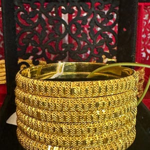 May include: A stack of five gold-coloured bangles with a textured, woven design.