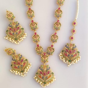 Può includere: Una collana d'oro con un ciondolo e orecchini abbinati. La collana e gli orecchini sono decorati con pietre colorate e perle.