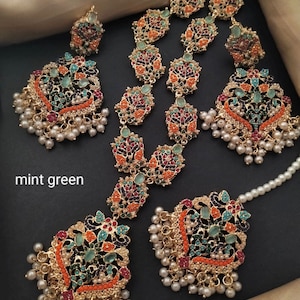 Könnte beinhalten: Ein Set aus goldfarbenem Schmuck mit bunten Steinen und Perlen. Das Set beinhaltet eine lange Halskette, ein Paar Ohrringe und ein Maang Tikka. Die Steine sind in Rot-, Orange-, Grün-, Blau- und Violetttönen gehalten. Die Perlen sind weiß. Der Schmuck liegt auf einem schwarzen Hintergrund. Der Text "mint green" ist im Bild sichtbar.