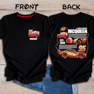 Op de afbeelding: Zwart T-shirt met een rode en gele cartoon raceauto aan de voorkant en een groter beeld van dezelfde auto met de tekst "Lightning McQueen" en "Est. 2005" op de achterkant.