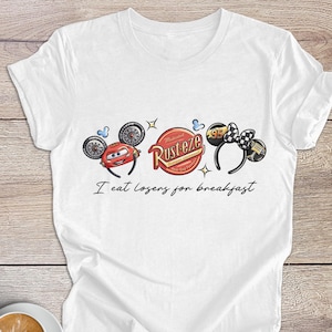 Peut inclure: T-shirt blanc avec un motif de voiture de dessin anim&eacute; et le texte "I eat losers for breakfast". Le design comprend une voiture rouge, un logo "Rusteze" et un n&oelig;ud papillon &agrave; carreaux noir et blanc.