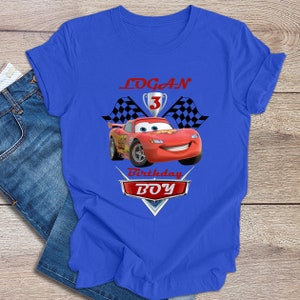 May include: Blue t-shirt featuring a red race car graphic, chequered flags, and the text "LOGAN 3 Birthday BOY".