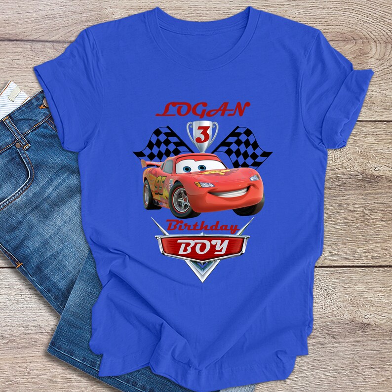 May include: Blue t-shirt featuring a red race car graphic, chequered flags, and the text "LOGAN 3 Birthday BOY".