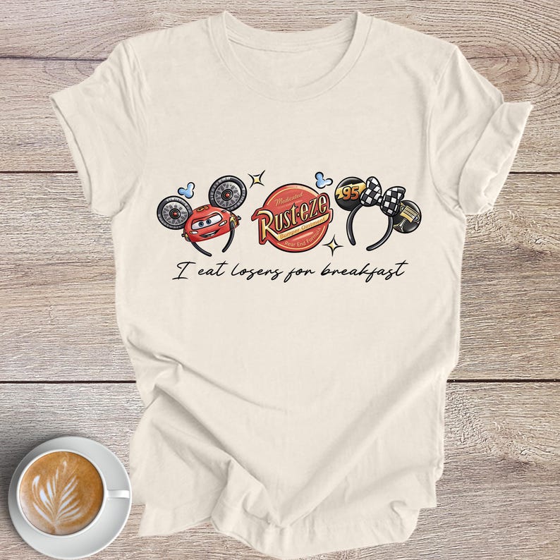 Peut inclure: T-shirt cr&egrave;me avec un motif sur le th&egrave;me de Cars. Le motif comprend des images de Flash McQueen, un logo Rust-eze et des oreilles de souris avec un n&oelig;ud &agrave; carreaux. Le texte "I eat losers for breakfast" est imprim&eacute; en dessous.
