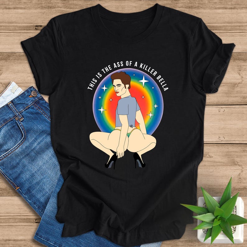 Peut inclure: T-shirt noir avec une illustration de dessin anim&eacute; d'une personne accroupie, portant une chemise bleue, des talons et des sous-v&ecirc;tements. Le motif est plac&eacute; sur un fond aux couleurs de l'arc-en-ciel avec des &eacute;toiles et le texte "THIS IS THE ASS OF A KILLER BELLA" en cercle.