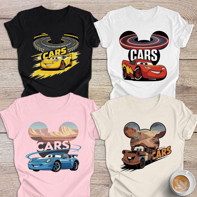 May include: Four t-shirts featuring "Cars" designs. The shirts are in black, white, pink, and beige. Each shirt displays a different car character and the word "Cars". The designs include race tracks and desert landscapes.