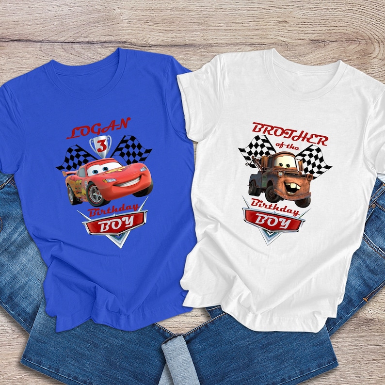 May include: Two blue and white t-shirts with a Cars theme. The blue shirt says "Logan 3 Birthday Boy" and features Lightning McQueen. The white shirt says "Brother of the Birthday Boy" and features Mater.