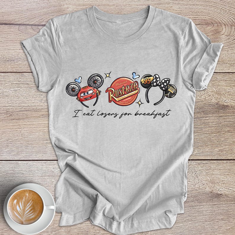 Peut inclure: Un t-shirt gris clair avec un motif graphique inspir&eacute; du film Cars. Le motif comprend des images de Flash McQueen, un logo "Rusteze" et un logo "95". Le texte "I eat losers for breakfast" est imprim&eacute; sous les graphiques.