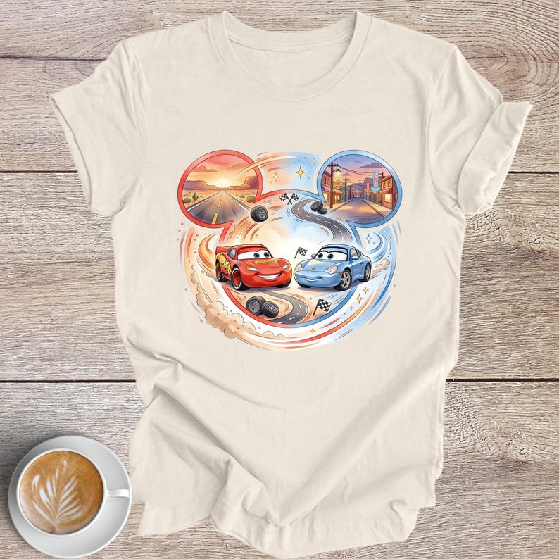 Peut inclure: T-shirt cr&egrave;me avec un motif color&eacute; de deux voitures de course de dessins anim&eacute;s, Flash McQueen et Sally Carrera, sur une piste. Le motif comprend un coucher de soleil et une sc&egrave;ne de ville, avec des drapeaux de course et des traces de pneus.