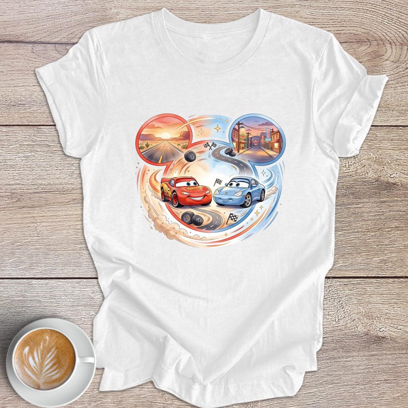 Peut inclure: T-shirt blanc avec un motif color&eacute; de deux voitures de course de dessins anim&eacute;s, une rouge et une bleue, sur un circuit. Le design comprend des sc&egrave;nes de coucher de soleil et de ville dans des cadres circulaires, avec des traces de pneus et des drapeaux &agrave; damier.