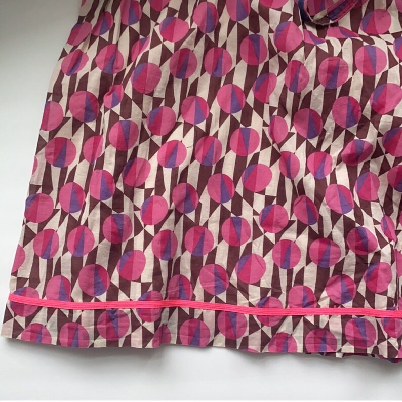 May include: A pink and purple geometric print skirt with a pink trim. The skirt is made of a lightweight fabric and has a flowy silhouette.