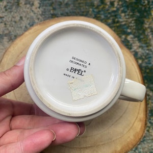 Może przedstawiać: Biały kubek ceramiczny z czarnym napisem "Designed & Decorated &copy; Papel&reg; Made in ".
