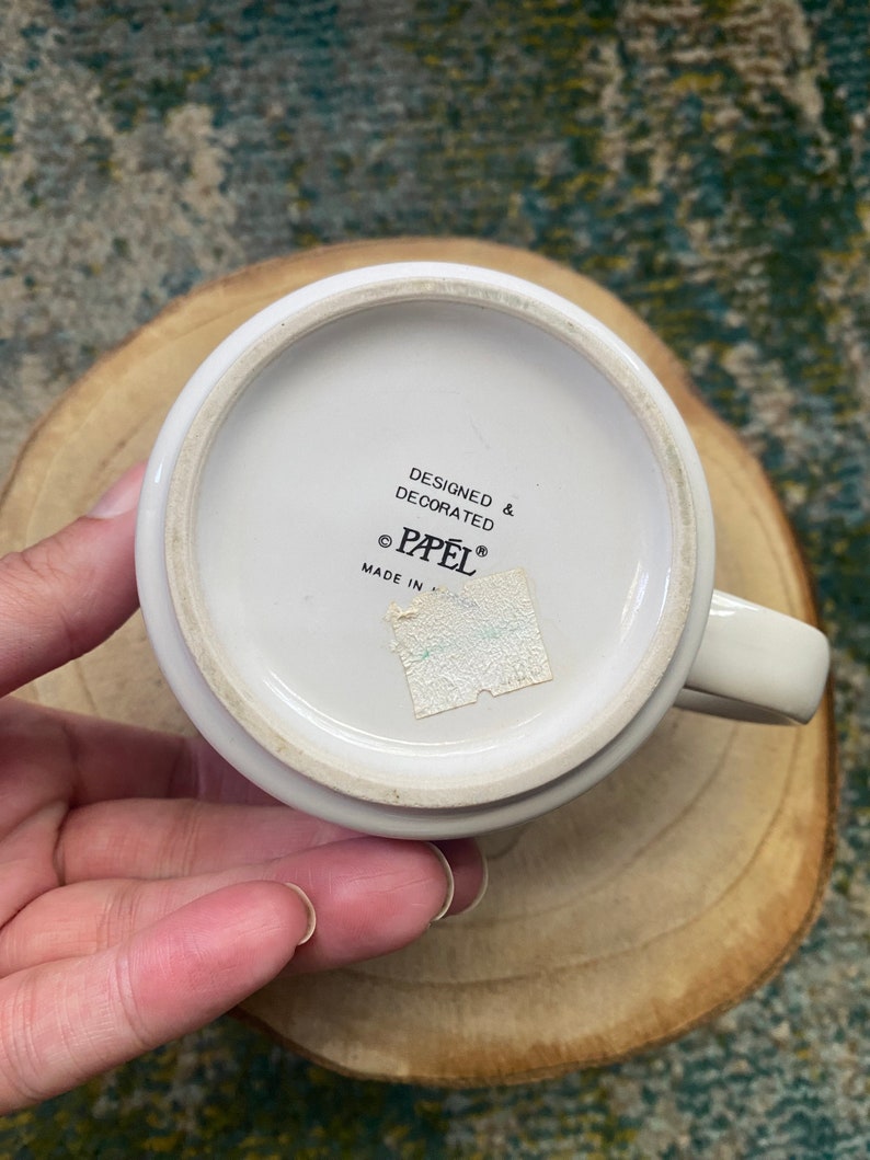 Może przedstawiać: Biały kubek ceramiczny z czarnym napisem "Designed & Decorated &copy; Papel&reg; Made in ".