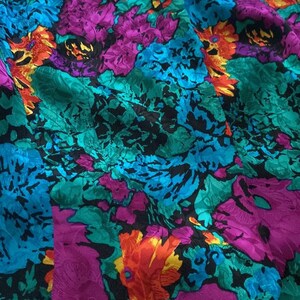 Puede incluir: Una tela vibrante con un patr&oacute;n floral en tonos de turquesa, morado, naranja y negro. La tela tiene una apariencia texturizada, casi arrugada.