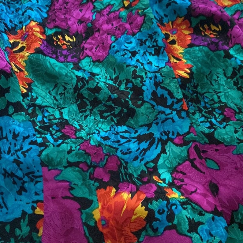 Puede incluir: Una tela vibrante con un patr&oacute;n floral en tonos de turquesa, morado, naranja y negro. La tela tiene una apariencia texturizada, casi arrugada.