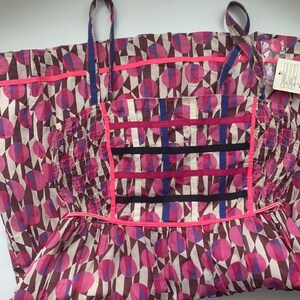 May include: A pink and brown dress with a geometric pattern of circles and triangles. The dress has a fitted bodice and a full skirt. The straps are adjustable.