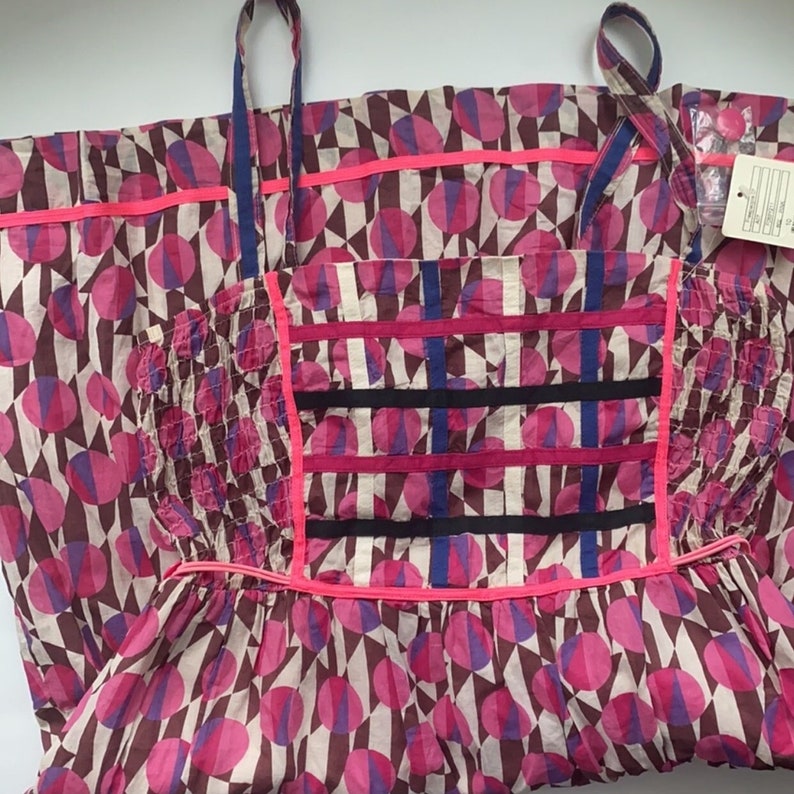 May include: A pink and brown dress with a geometric pattern of circles and triangles. The dress has a fitted bodice and a full skirt. The straps are adjustable.