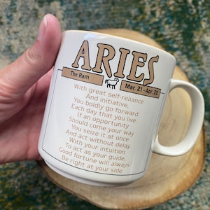 Może przedstawiać: Biały ceramiczny kubek z brązowo-złotym wzorem przedstawiającym znak zodiaku Baran. Kubek ma uchwyt i napis "The Ram" oraz "Mar. 21-Apr. 20". Tekst brzmi: "Z wielką pewnością siebie i inicjatywą. Odważnie idziesz naprz&oacute;d każdego dnia swojego życia. Jeśli nadarzy się okazja, chwytasz ją natychmiast i działasz bez zwłoki. Z intuicją jako przewodnikiem. Szczęście zawsze będzie po twojej stronie."