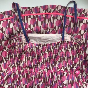 May include: A pink and brown patterned dress with a gathered bodice and thin straps. The dress has a pink and white geometric pattern with circles.