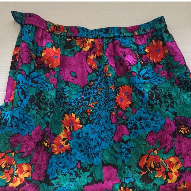 Puede incluir: Una falda floral colorida con fondo negro. La falda tiene una mezcla vibrante de flores rosas, azules, verdes, naranjas y amarillas.