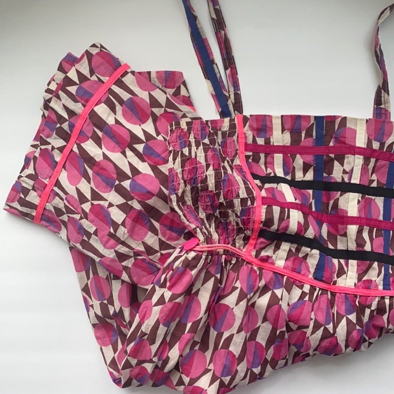 May include: A pink and brown patterned dress with pink and blue circles and black and white stripes. The dress has thin pink straps and a gathered bodice.