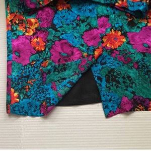 Puede incluir: Una tela de estampado floral colorido con forro negro. La tela tiene un estampado floral rosa, azul, verde y amarillo.