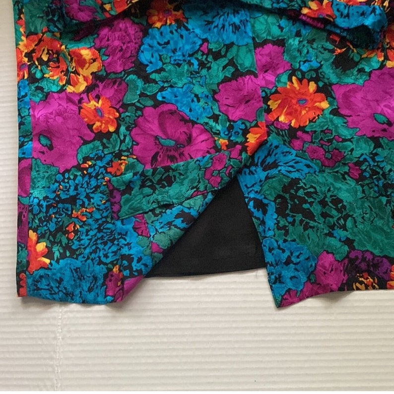Puede incluir: Una tela de estampado floral colorido con forro negro. La tela tiene un estampado floral rosa, azul, verde y amarillo.