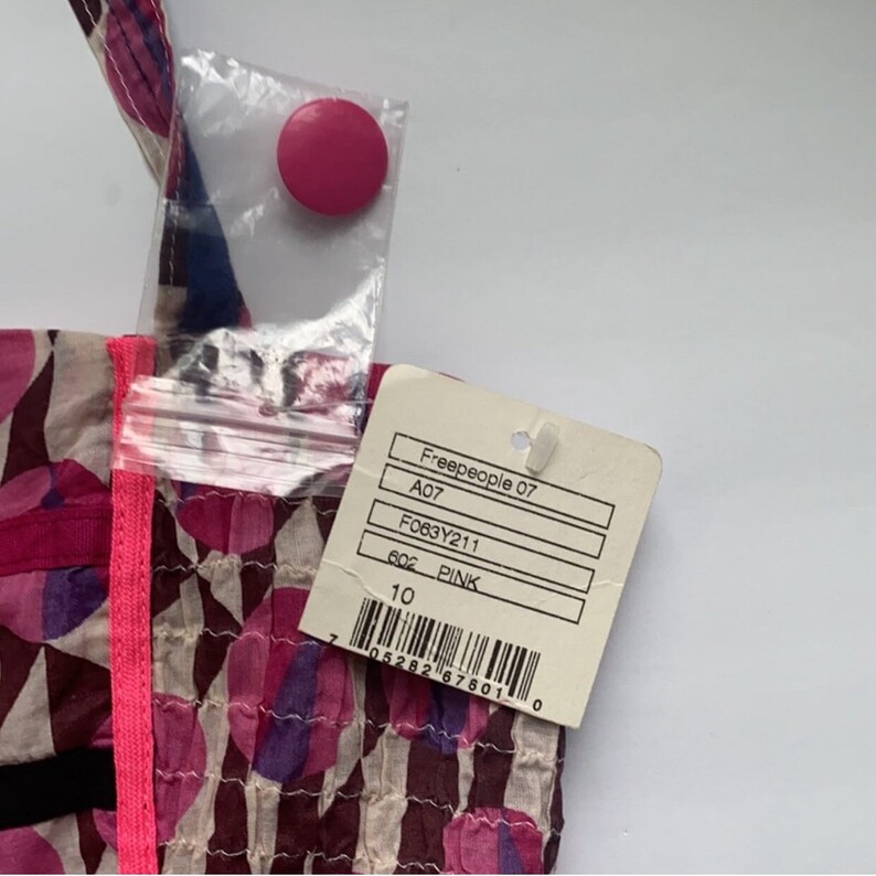 May include: A pink and white patterned fabric bag with a pink zipper pull and a Freepeople tag. The tag has the following information: Freepeople 07, A07, F063Y211, 6oz PINK, 10, 7 05282 67801 0