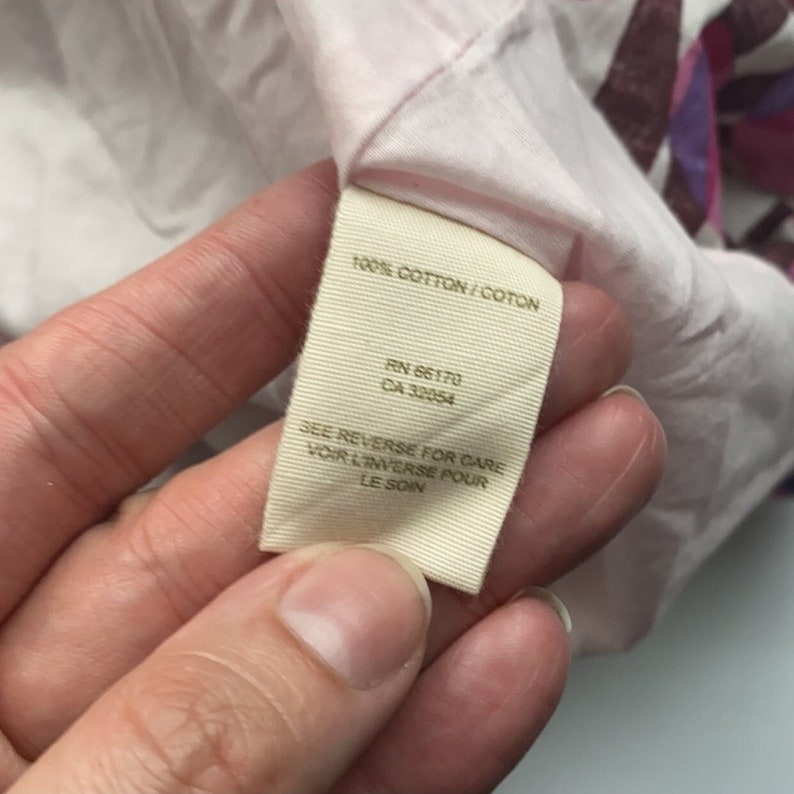 May include: A white tag with brown text that reads "100% COTTON/COTON", "RN 66170", "CA 32054", "SEE REVERSE FOR CARE", "VOIR L'INVERSE POUR LE SOIN".