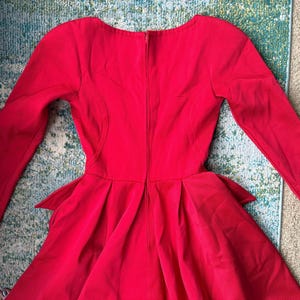 May include: A red long-sleeved dress with a fitted bodice and a flared skirt. The dress has a back zipper and a high neckline.