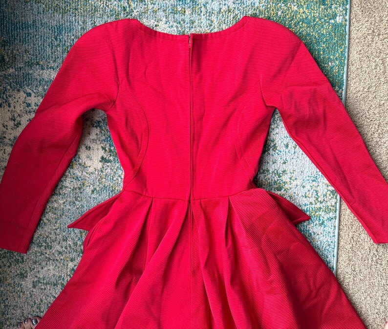 May include: A red long-sleeved dress with a fitted bodice and a flared skirt. The dress has a back zipper and a high neckline.