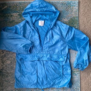 May include: A light blue hooded windbreaker jacket with a zipper closure and a kangaroo pocket. The jacket has a drawstring hood and elastic cuffs.