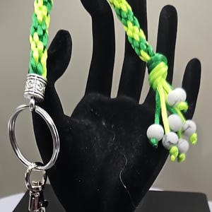 May include: A green and yellow braided keychain with a silver key ring and a white bead tassel.