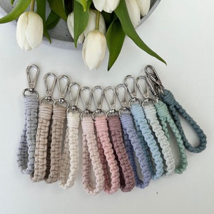 Könnte beinhalten: Ein Set aus zehn bunten Makramee-Schlüsselanhängern mit silbernen Schlüsselringen. Die Schlüsselanhänger sind in verschiedenen Farben gefertigt, darunter Blau, Grün, Rosa und Beige.