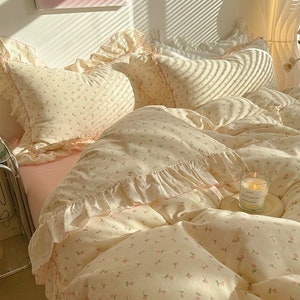 May include: A white and pink floral bedding set with a ruffled edge. The bedding is made of soft, comfortable fabric and features a delicate floral pattern. The set includes a duvet cover, two pillowcases, and a decorative throw pillow.