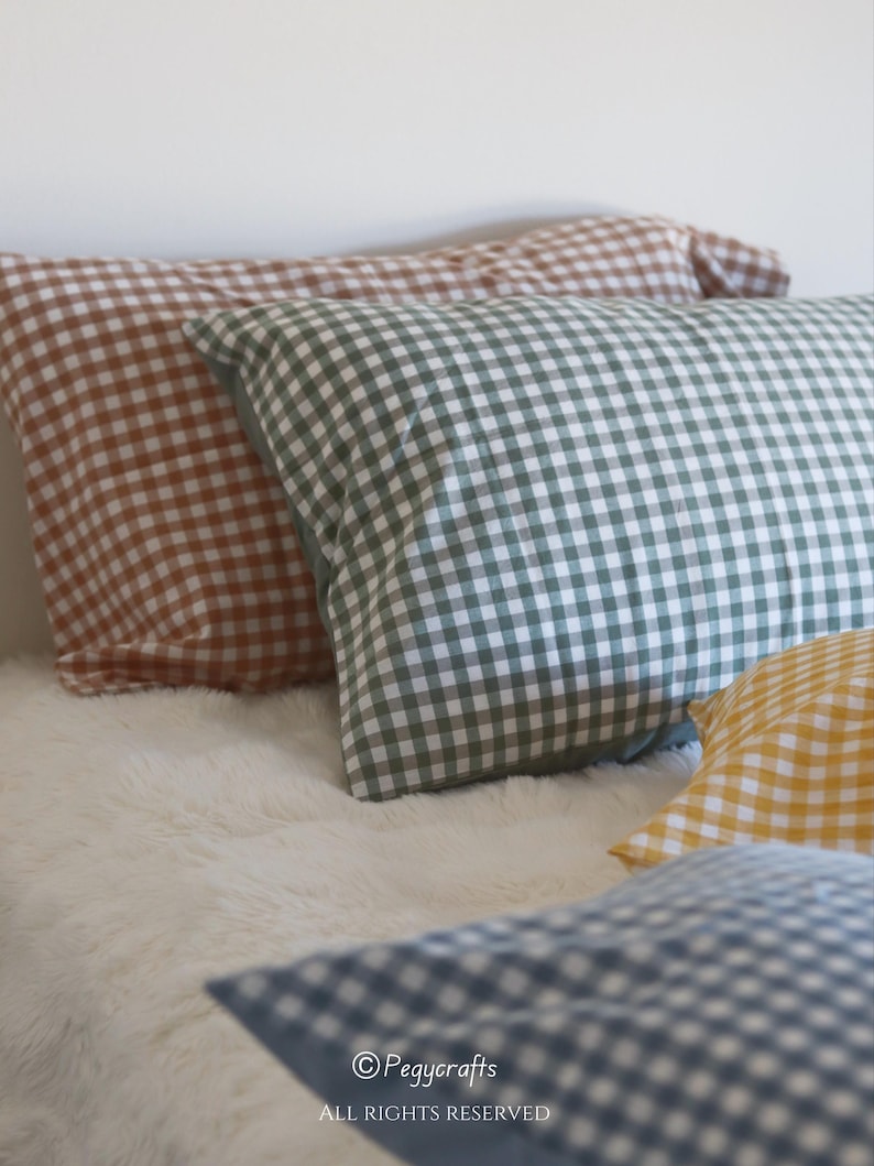 May include: Several gingham-patterned pillowcases in shades of brown, green, yellow, and blue rest on a white, fluffy surface. The pillowcases are rectangular and feature a classic checkered design. The image is well-lit, showcasing the various colors and textures.